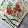 Four small glasses on a decorative towel with tomato design