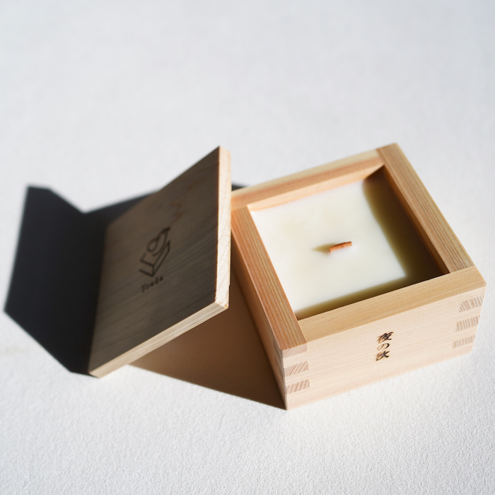 Candle in a wooden box with a visible brand logo on a light background